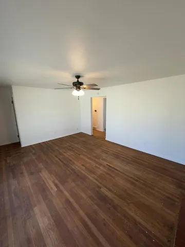 an empty room with wooden floor fan and windows