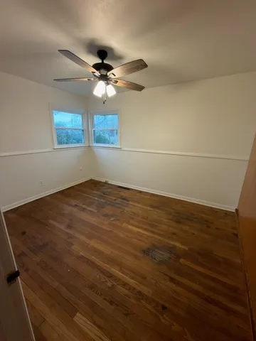 an empty room with wooden floor fan and windows
