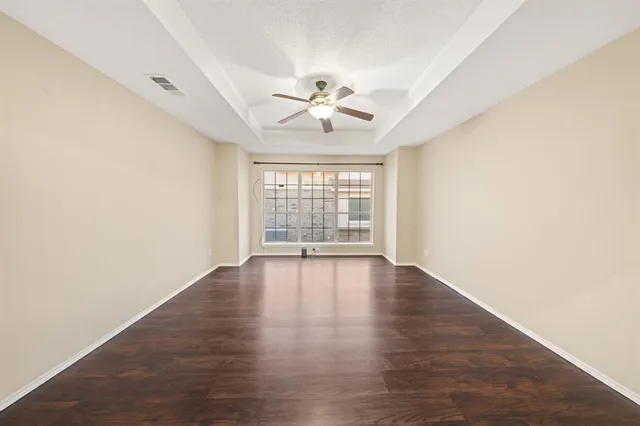 an empty room with wooden floor chandelier fan and windows