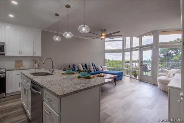 a view of a kitchen with granite countertop a stove a sink a large window with chairs and wooden floor