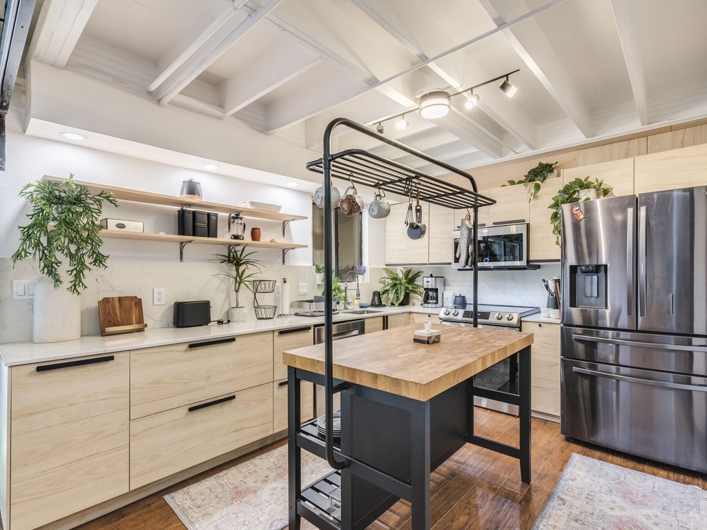 Kitchen featuring light wood finish cabinetry, modern cabinets, stainless steel appliances, tasteful backsplash, and beam ceiling