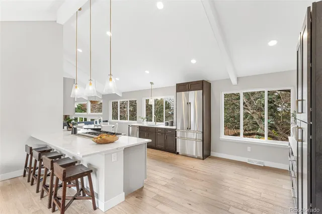 a room with stainless steel appliances kitchen island granite countertop a stove a refrigerator a sink a dining table and chairs with wooden floor