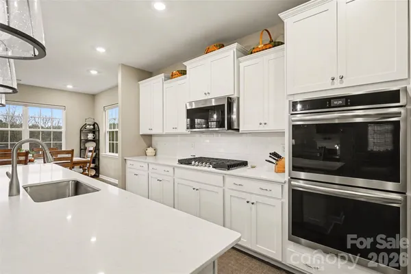 a kitchen with granite countertop a sink dishwasher stove and white cabinets with wooden floor