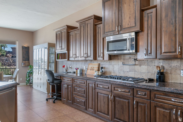 2376 Stone Crest Circle St. George, UT 84790 - Photo 13 of 61 Kitchen featuring stainless steel appliances, dark wood finish cabinetry, dark stone countertops, and decorative backsplash