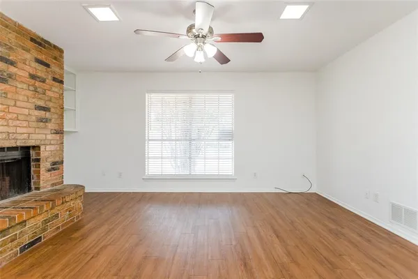 an empty room with wooden floor chandelier fan and windows