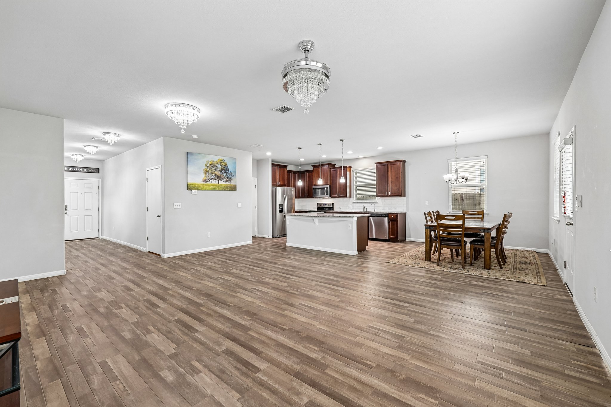387 Guemal Road Buda, TX 78610 - Photo 5 of 39 Open-concept living area featuring wood-finish flooring, a kitchen island with seating, dark wood cabinetry, stainless steel appliances, and multiple ceiling-mounted light fixtures