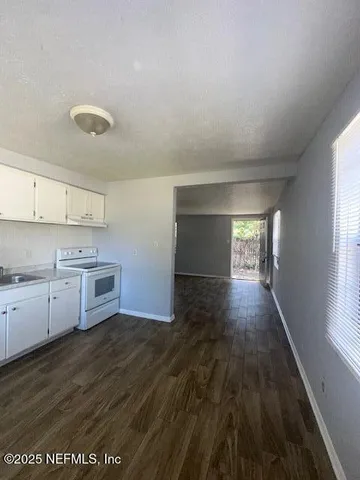 a kitchen with granite countertop a stove a sink and white cabinets with wooden floor
