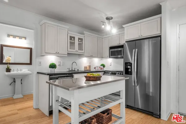 a kitchen with stainless steel appliances a stove a sink a refrigerator white cabinets and wooden floor