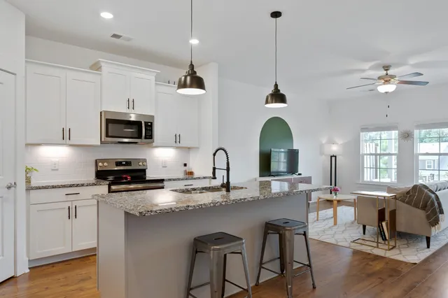 a kitchen with stainless steel appliances granite countertop a stove a sink dishwasher a microwave oven with white cabinets and wooden floor