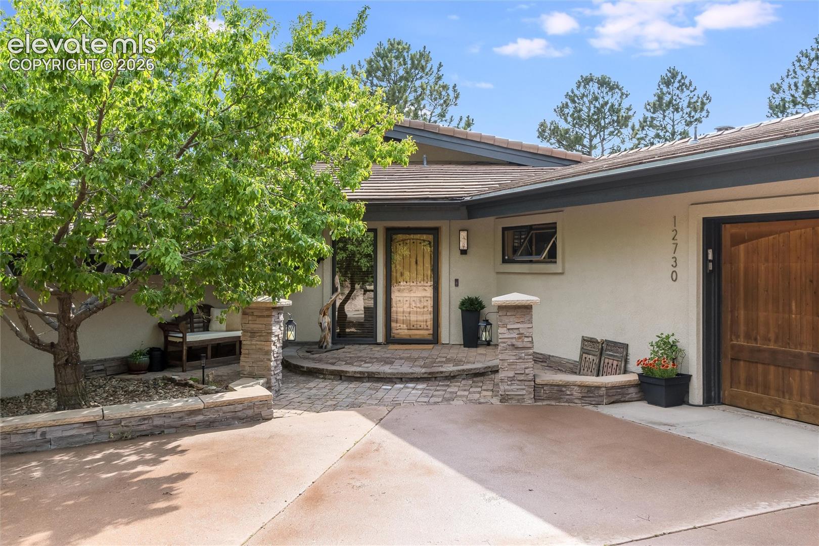 12730 Bridle Bit Road Colorado Springs, CO 80908 - Photo 45 of 48 Front entrance featuring a rich wood door, stone facade accents, and a paved entry