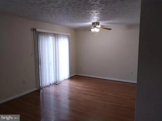 an empty room with wooden floor chandelier fan and windows