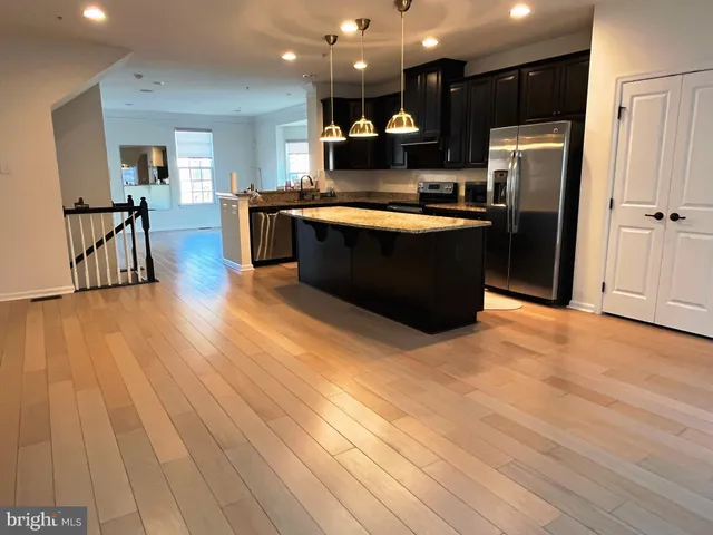 a kitchen with stainless steel appliances granite countertop a refrigerator a sink dishwasher a stove and a dining table with wooden floor