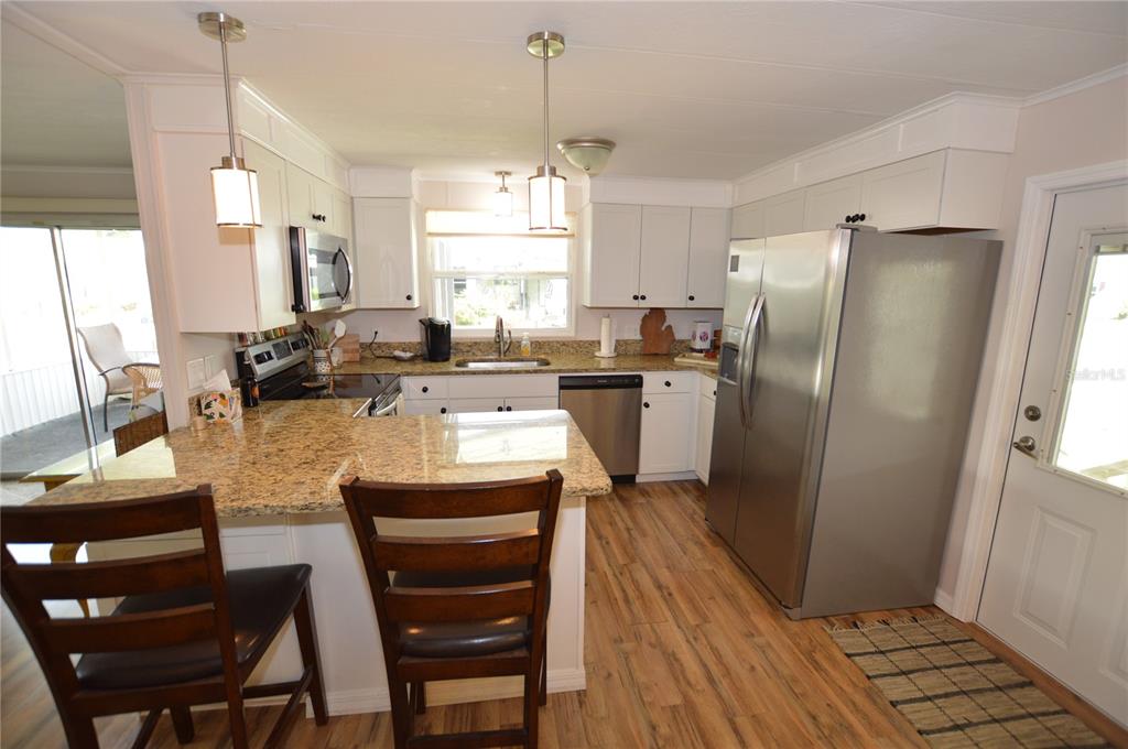 140 Rarotonga Road North Port, FL 34287 - Photo 7 of 42 a kitchen with stainless steel appliances granite countertop a refrigerator a stove a sink dishwasher a dining table and chairs with wooden floor