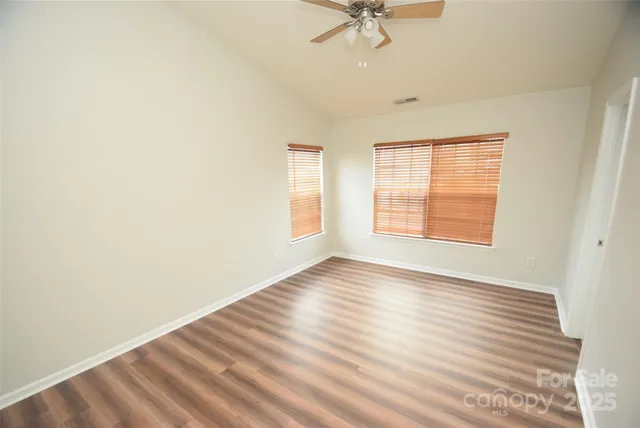 an empty room with wooden floor chandelier fan and windows