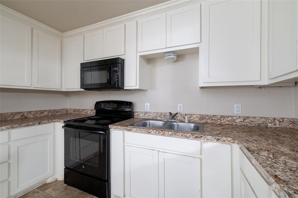 313 North Roe Street White Settlement, TX 76108 - Photo 11 of 33 Kitchen featuring white cabinetry with crown molding, black freestanding range, coordinating black over-the-range microwave, double basin stainless steel sink, and speckled countertops