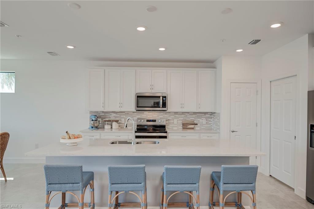 5686 Mayflower Way, Unit 702 Ave Maria, FL 34142 - Photo 16 of 50 Kitchen featuring a quartz counters, tiled backsplash, & stainless steel appliances, white cabinetry