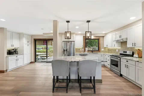 a kitchen with stainless steel appliances granite countertop a stove top oven a sink dishwasher and white cabinets with wooden floor