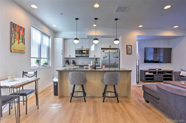 a kitchen with stainless steel appliances kitchen island granite countertop a stove a sink a refrigerator a stove a dining table and chairs with wooden floor