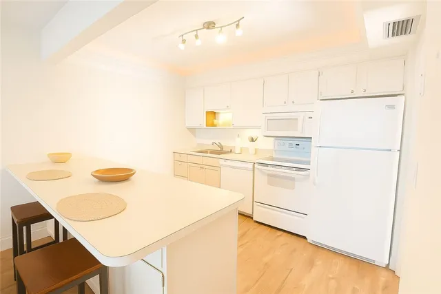 a white kitchen with a stove a refrigerator a sink a dining table and chairs
