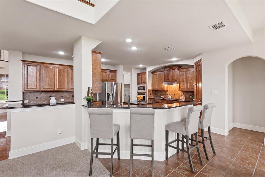 2841 Meadow Ridge Drive Prosper, TX 75078 - Photo 12 of 40 a kitchen with kitchen island granite countertop wooden cabinets and stainless steel appliances
