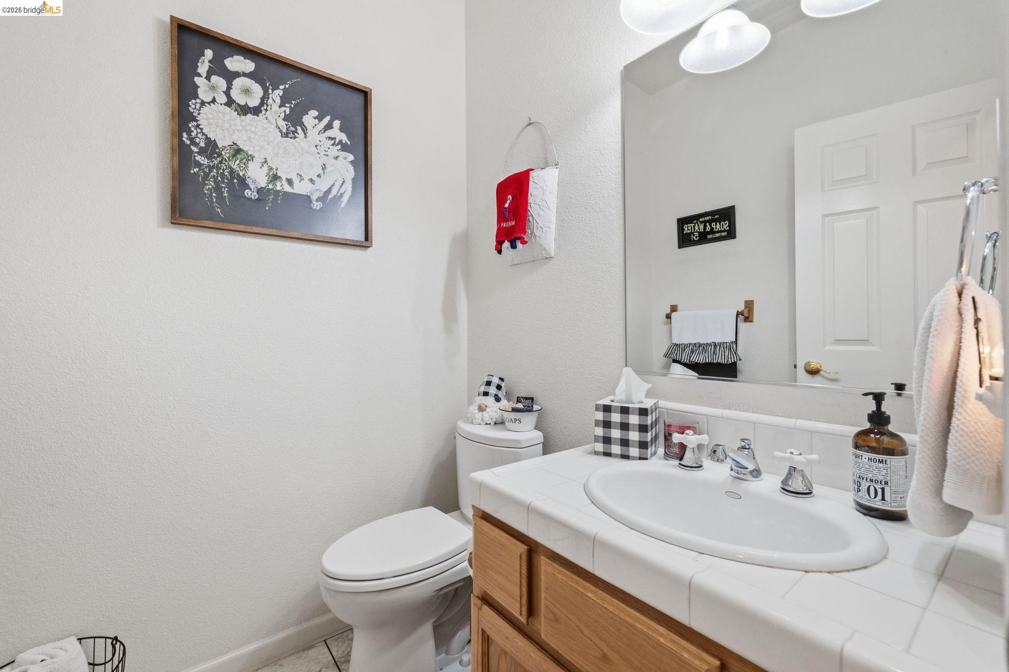 18450 Lambert Lake Road Sonora, CA 95370 - Photo 28 of 87 Bathroom featuring a white drop-in sink, tile countertop, light wood-finish vanity, and a wall-mounted mirror