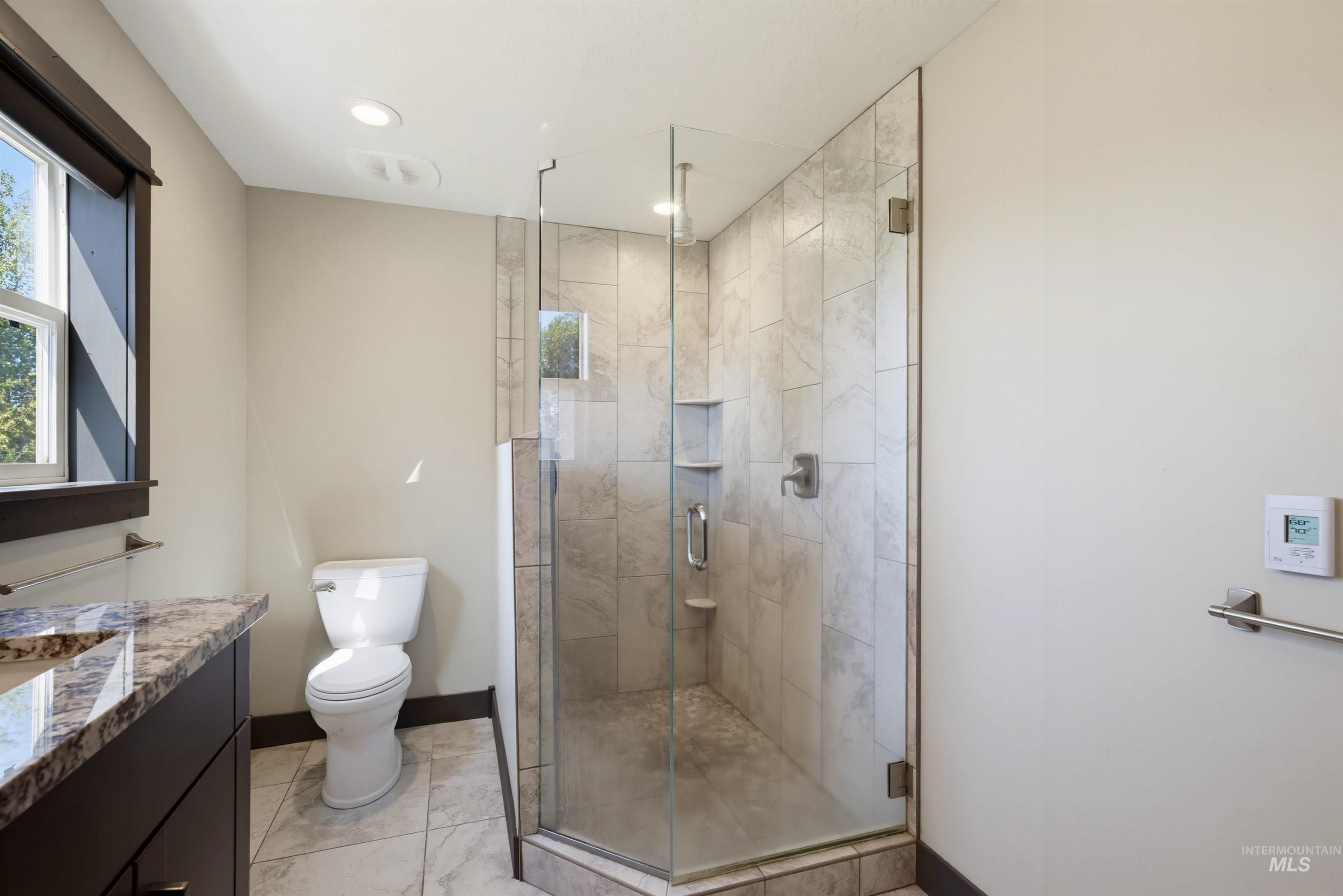 13945 Galloping Road McCall, ID 83638 - Photo 22 of 50 Glass-enclosed shower with tiled walls and built-in shelving, complemented by a dark wood-finish vanity with a stone countertop and an undermount sink