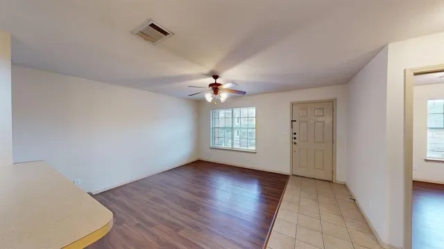 an empty room with wooden floor chandelier fan and windows