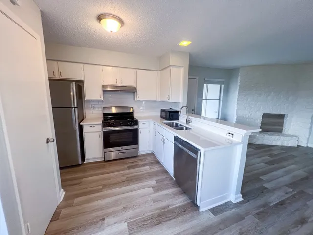 a kitchen with stainless steel appliances a stove a refrigerator a sink a stove with wooden floor