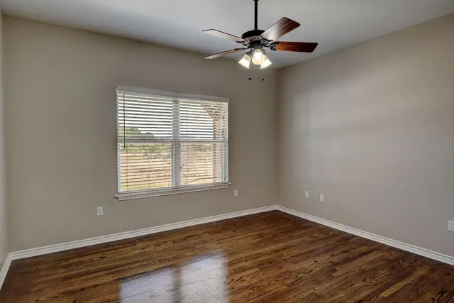 an empty room with wooden floor fan and windows