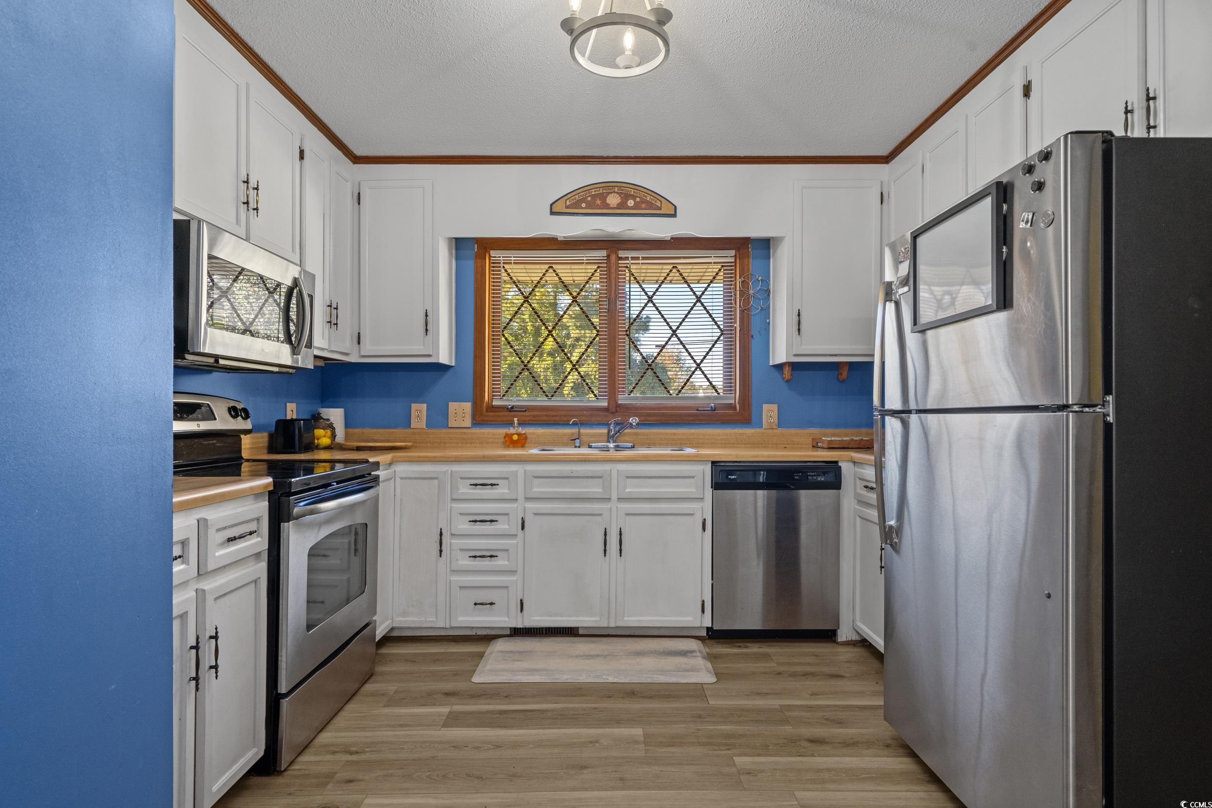 1063 Burcale Road Myrtle Beach, SC 29579 - Photo 16 of 36 Kitchen with stainless steel appliances, light countertops, light wood-style flooring, white cabinetry, and a textured ceiling