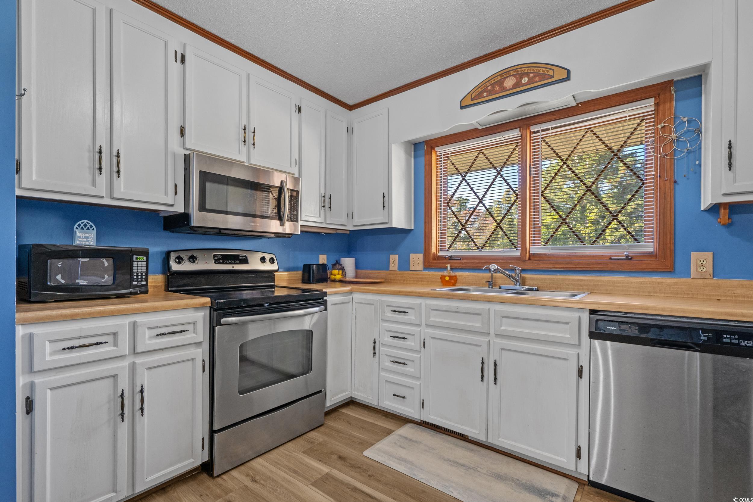 1063 Burcale Road Myrtle Beach, SC 29579 - Photo 17 of 36 Kitchen featuring appliances with stainless steel finishes, light countertops, white cabinets, light wood-style flooring, and ornamental molding