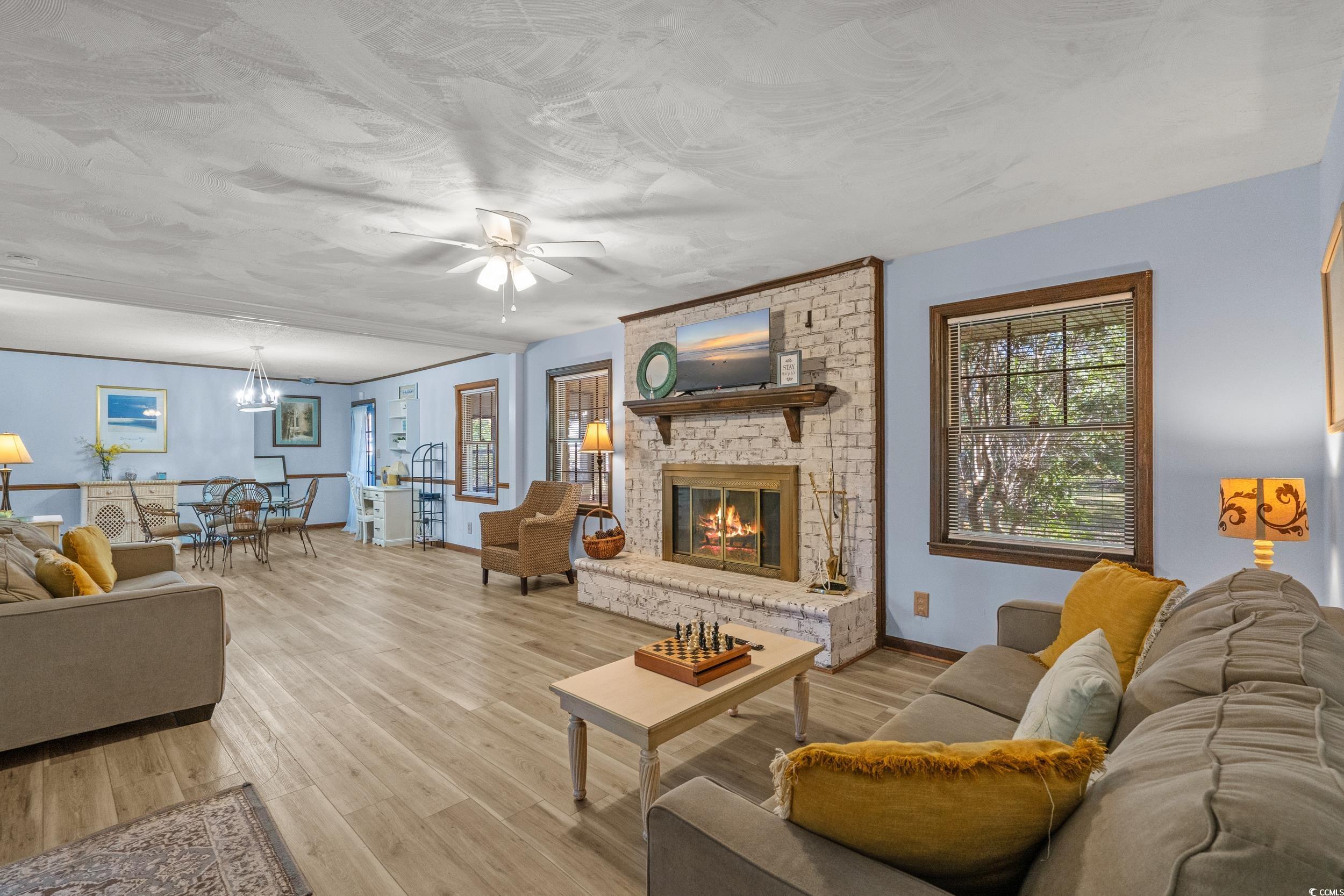 1063 Burcale Road Myrtle Beach, SC 29579 - Photo 10 of 36 Living room featuring light wood-style flooring, ceiling fan, a brick fireplace, and a chandelier