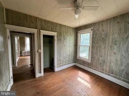 an empty room with wooden floor chandelier fan and windows