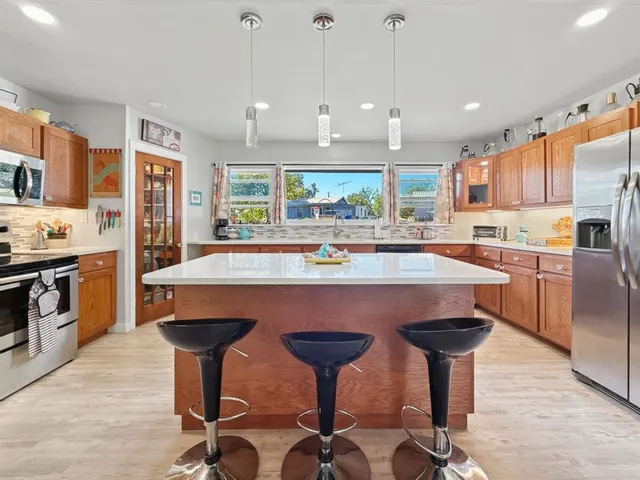 a kitchen with stainless steel appliances granite countertop a sink a stove a refrigerator and chairs