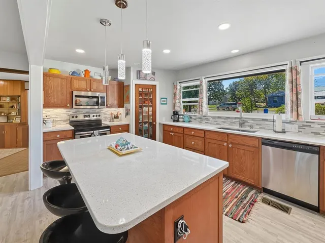 a kitchen with stainless steel appliances granite countertop a sink a stove a refrigerator and white cabinets with wooden floor