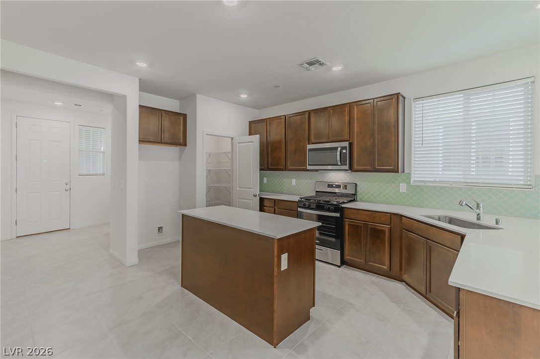 3765 Osiris Avenue Henderson, NV 89044 - Photo 5 of 40 Kitchen with stainless steel appliances, a center island, light tile patterned flooring, recessed lighting, and light stone counters