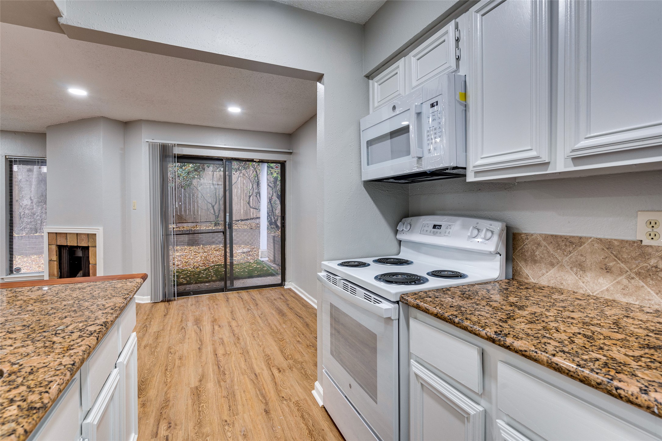 1808 Rio Grande Street, Unit 6 Austin, TX 78701 - Photo 11 of 29 Kitchen with white appliances, light stone counters, light wood-style floors, white cabinets, and a tiled fireplace