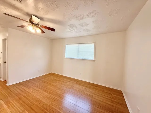 an empty room with wooden floor ceiling fan and windows