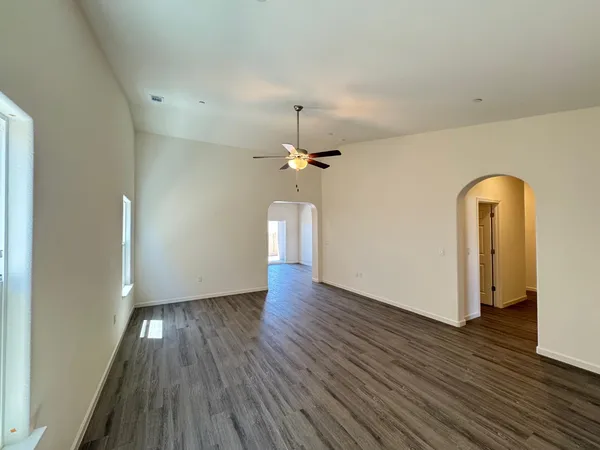 an empty room with wooden floor chandelier fan and windows