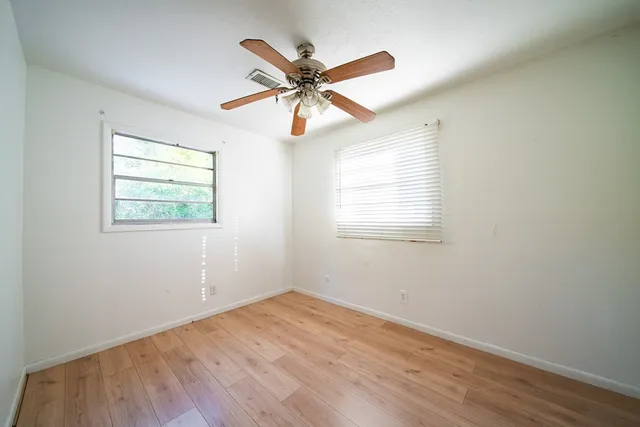an empty room with wooden floor ceiling fan and windows