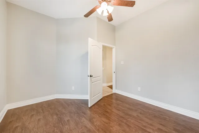 an empty room with wooden floor fan and windows
