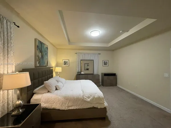 a spacious bedroom with a bed and a lamp on dresser