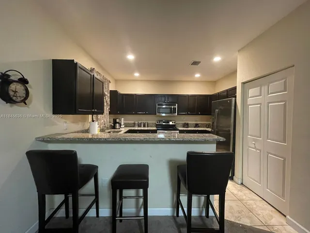 a kitchen with stainless steel appliances granite countertop a sink a stove a refrigerator and white cabinets with wooden floor