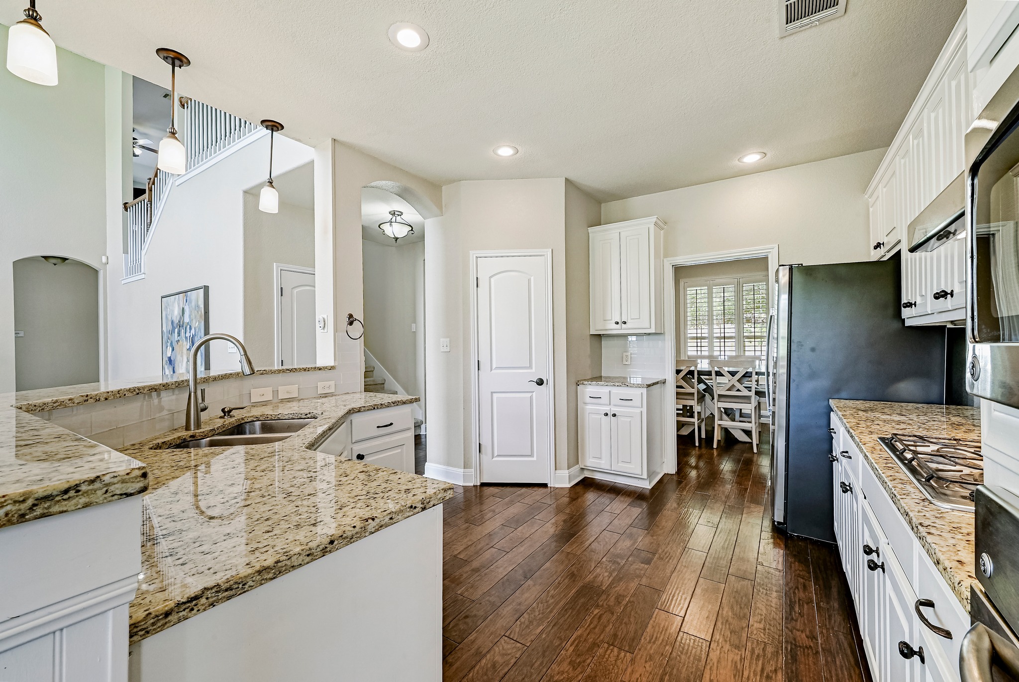 2408 Amen Corner Road Pflugerville, TX 78660 - Photo 13 of 40 Kitchen featuring wood-finish flooring, light-toned granite countertops, white cabinetry with dark hardware, and recessed lighting