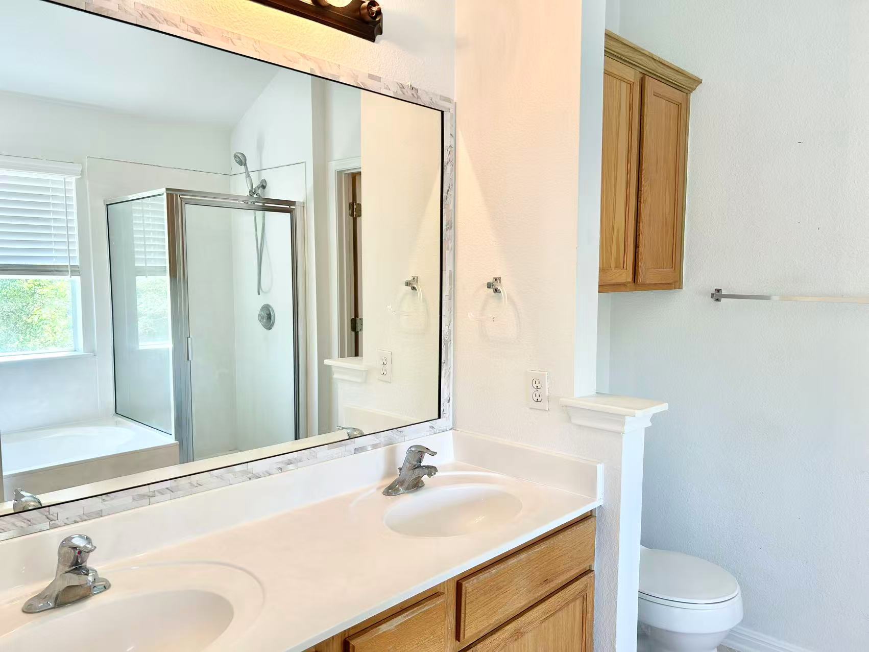 5608 Netleaf Road Austin, TX 78724 - Photo 19 of 26 Dual vanities complement a bright bathroom featuring a glass-enclosed shower and a separate toilet area.
