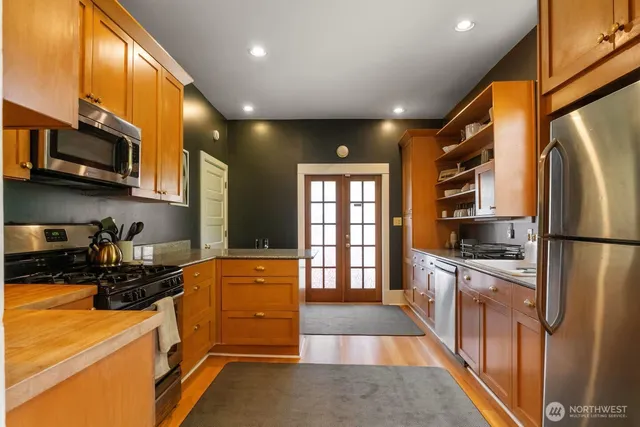 a kitchen with stainless steel appliances granite countertop a refrigerator a stove and a sink with wooden floor