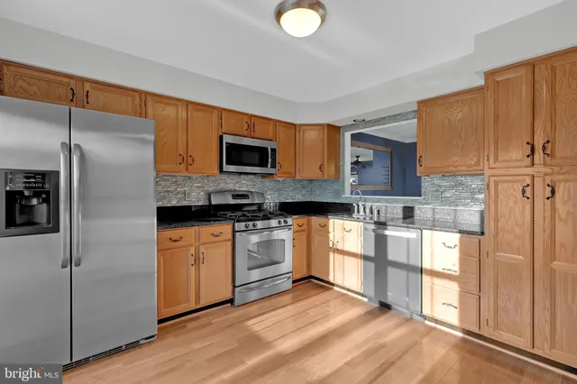 a kitchen with stainless steel appliances granite countertop a refrigerator a stove and a sink with wooden floor