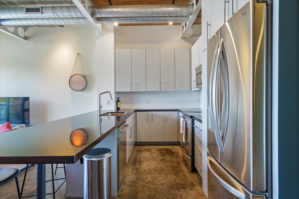 1401 Eva Street, Unit 302 Austin, TX 78704 - Photo 6 of 15 Kitchen featuring stainless steel appliances, a peninsula, concrete floors, a kitchen bar, and decorative backsplash