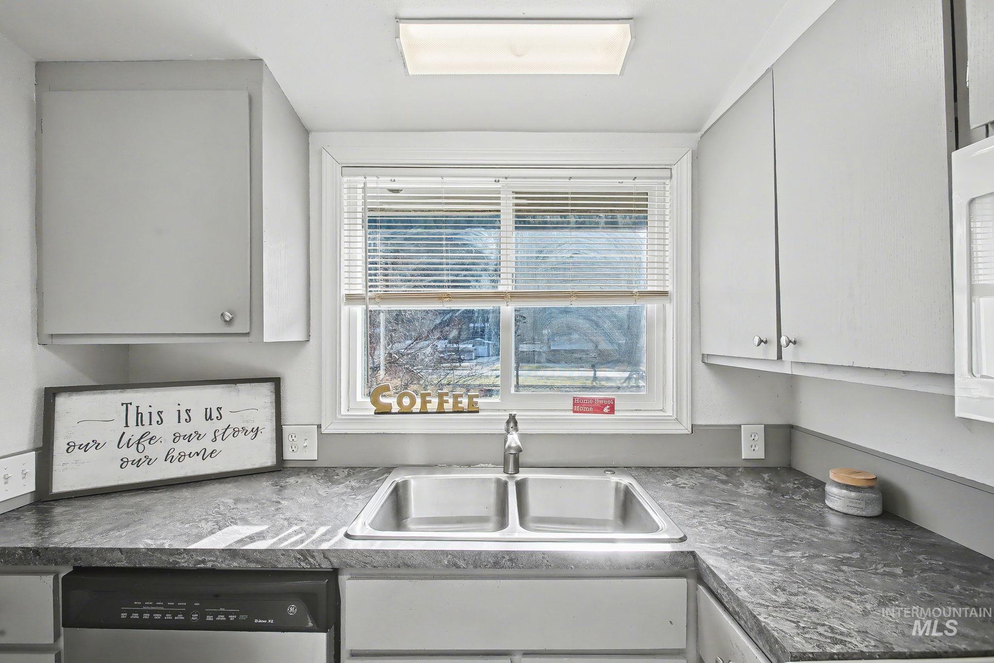 150 Elm Street Orofino, ID 83544 - Photo 6 of 36 Kitchen featuring a double basin stainless steel sink, a window with blinds, light gray cabinetry, dark patterned countertops, and a built-in dishwasher