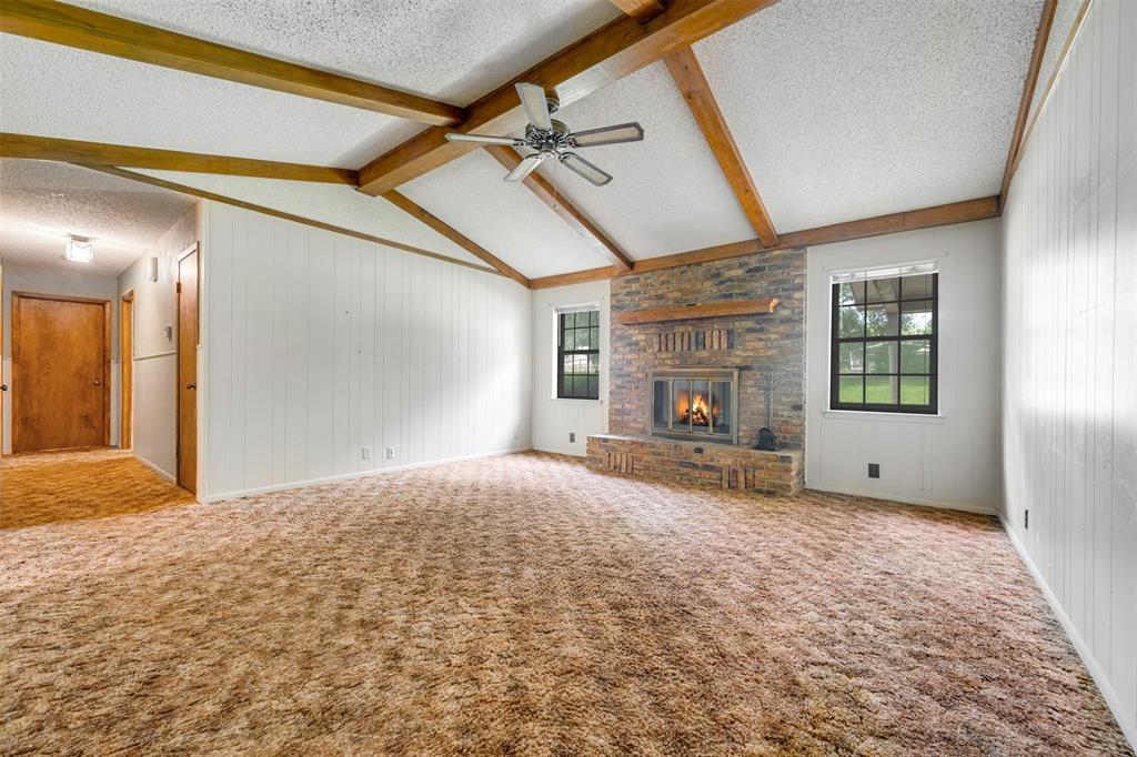 8798 Hill N Dale Road Tyler, TX 75709 - Photo 6 of 31 Spacious living area featuring a vaulted ceiling with exposed wood beams, a brick-surround fireplace with a wood mantle, and paneled walls